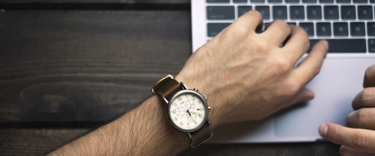 A person wearing a watch and typing on a laptop keyboard