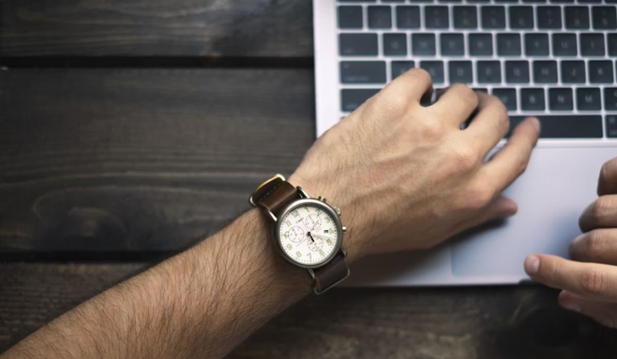 A person wearing a watch and typing on a laptop keyboard