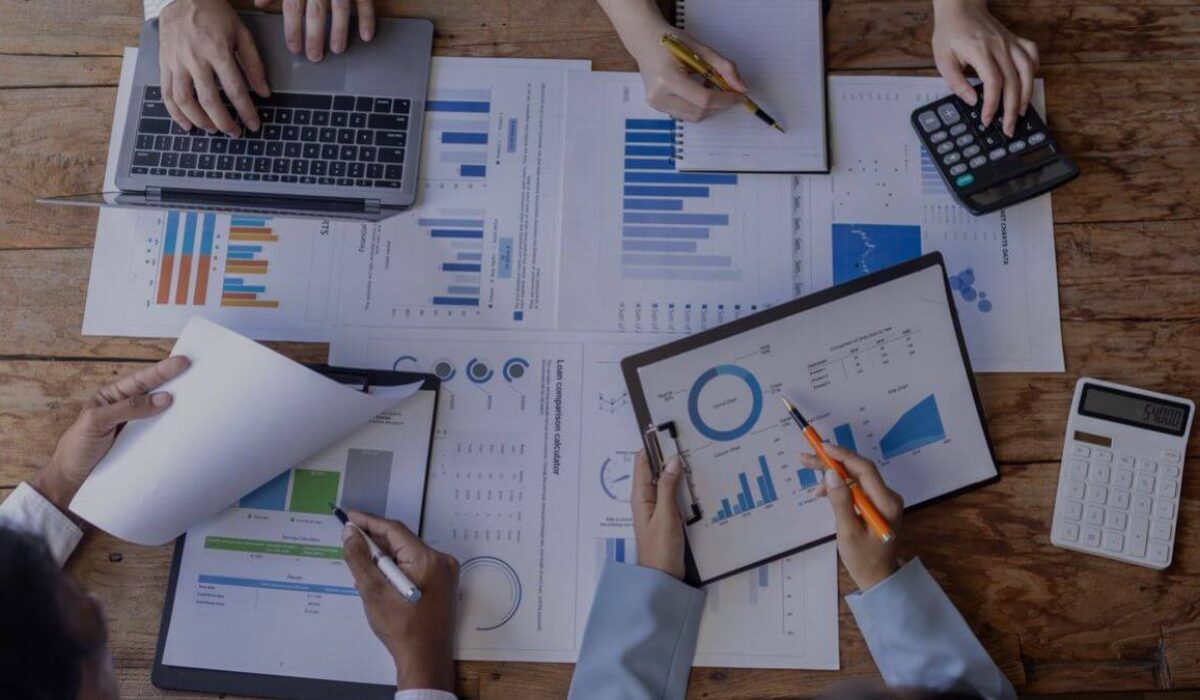 Bar charts, pie charts documents scattered on the table and employees trying to analyse them